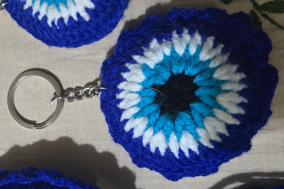 Scalloped-edge crochet evil-eye keychain lying next to its key ring