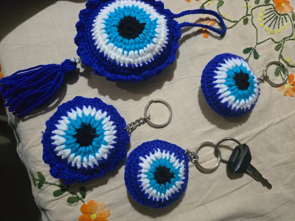 Several blue crochet evil-eye keychains with metal rings and a car key, on an embroidered cloth