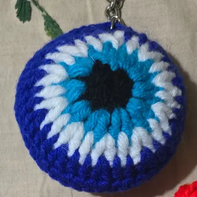 Round crochet evil-eye keychain in royal blue, white and sky blue with a black centre, on a metal key ring