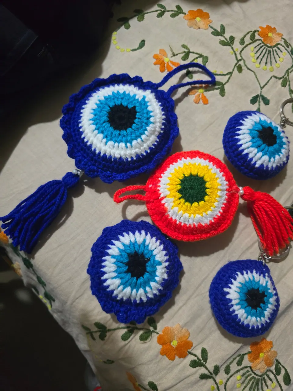 Blue tassel crochet evil-eye charm shown with smaller evil-eye keychains and a red evil-eye charm