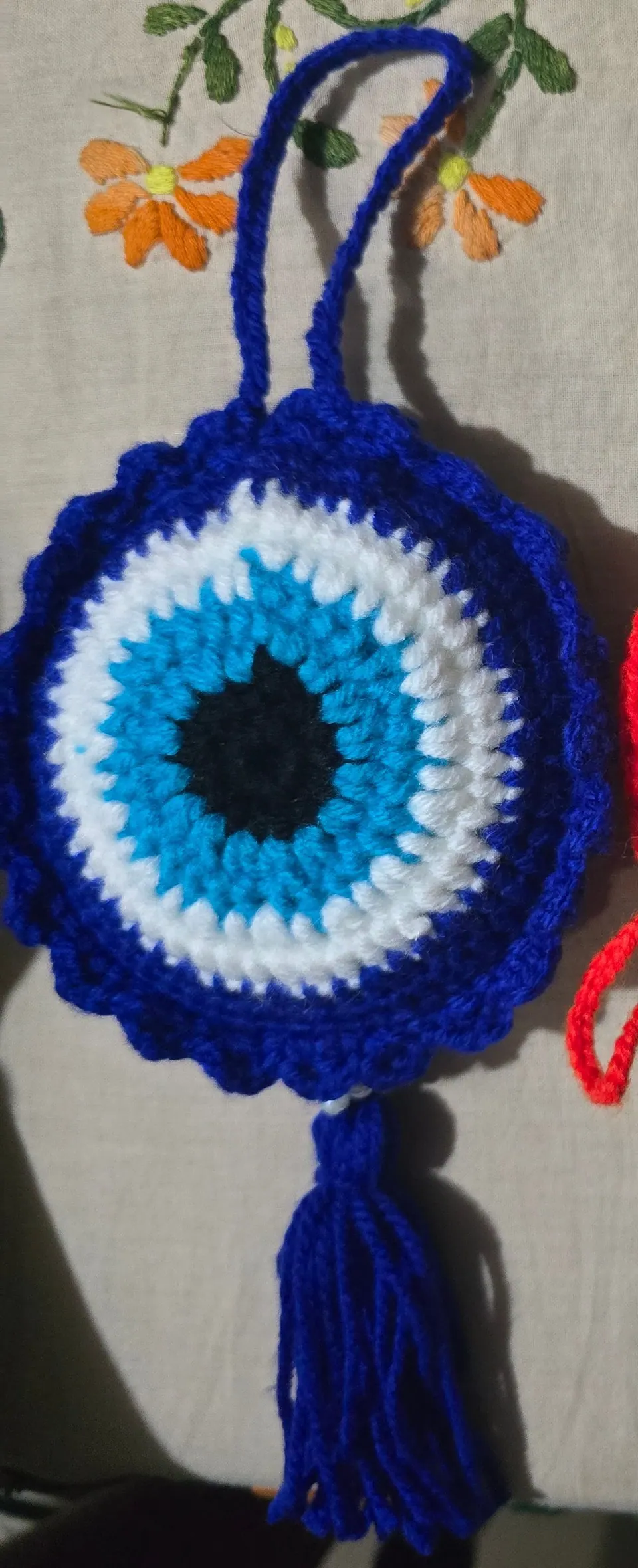 Large blue crochet evil-eye charm with a scalloped edge, yarn hanging loop and blue tassel