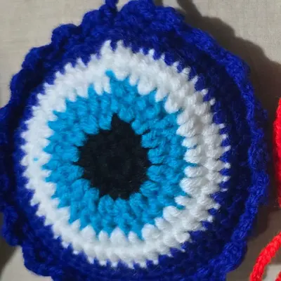 Large blue crochet evil-eye charm with a scalloped edge, yarn hanging loop and blue tassel