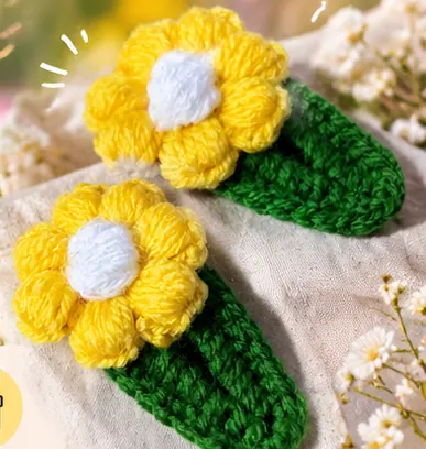 Two yellow crochet flower hair clips with green leaves on a cream cloth (illustrative image)