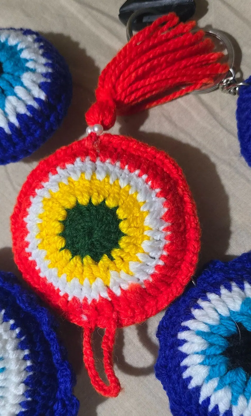 Red crochet evil-eye charm with white and yellow rounds, dark green centre, red yarn loop and red tassel
