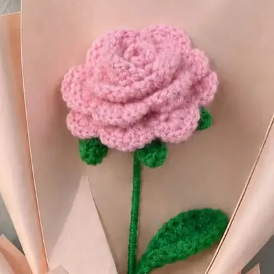 Pink crochet rose bouquet wrapped in blush paper with a white ribbon bow, standing on a wooden table