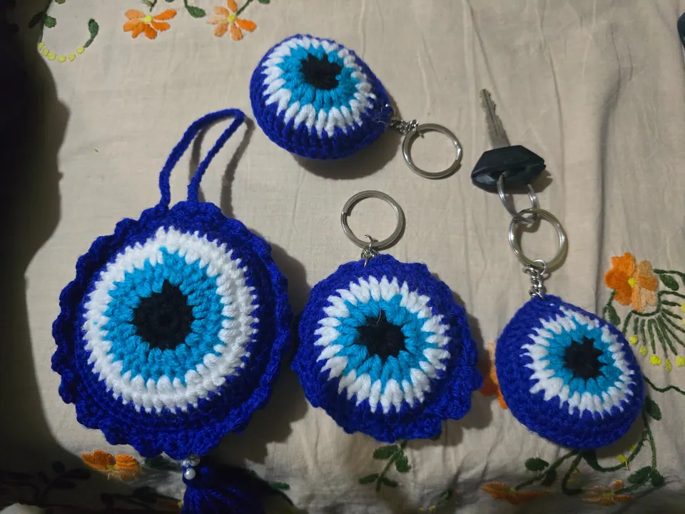 Crochet evil-eye keychains with metal key rings and a large tassel charm on an embroidered cloth